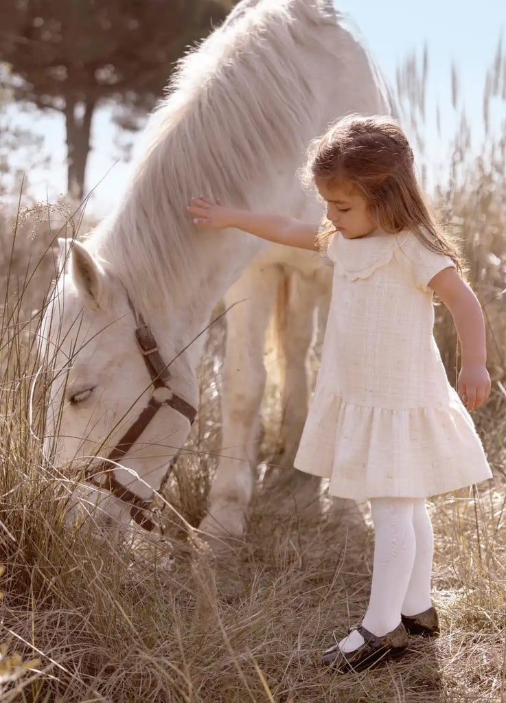 Un poney blanc étant doucement touché par un enfant dans une robe blanche.