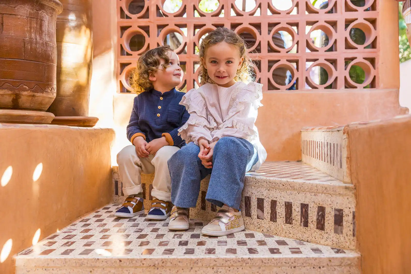 Deux enfants assis ensemble sur des marches carrelées en vêtements décontractés.