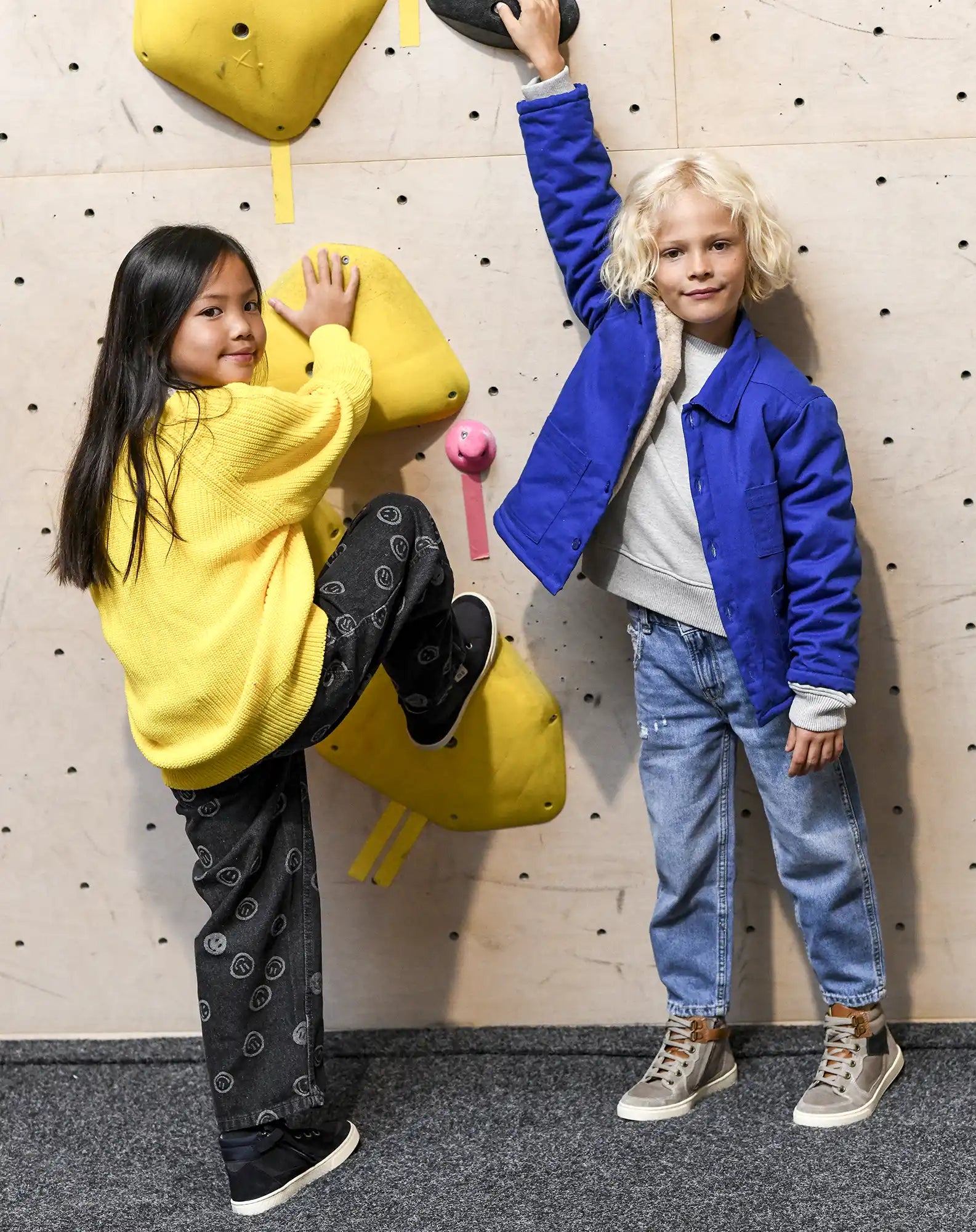 Deux enfants grimpent sur un mur d'escalade intérieur avec des prises jaunes.