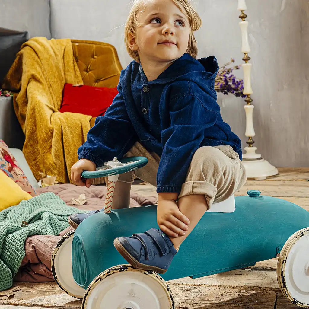 Un enfant portant un sweat à capuche bleu marine et un pantalon kaki est assis sur un coussin turquoise.