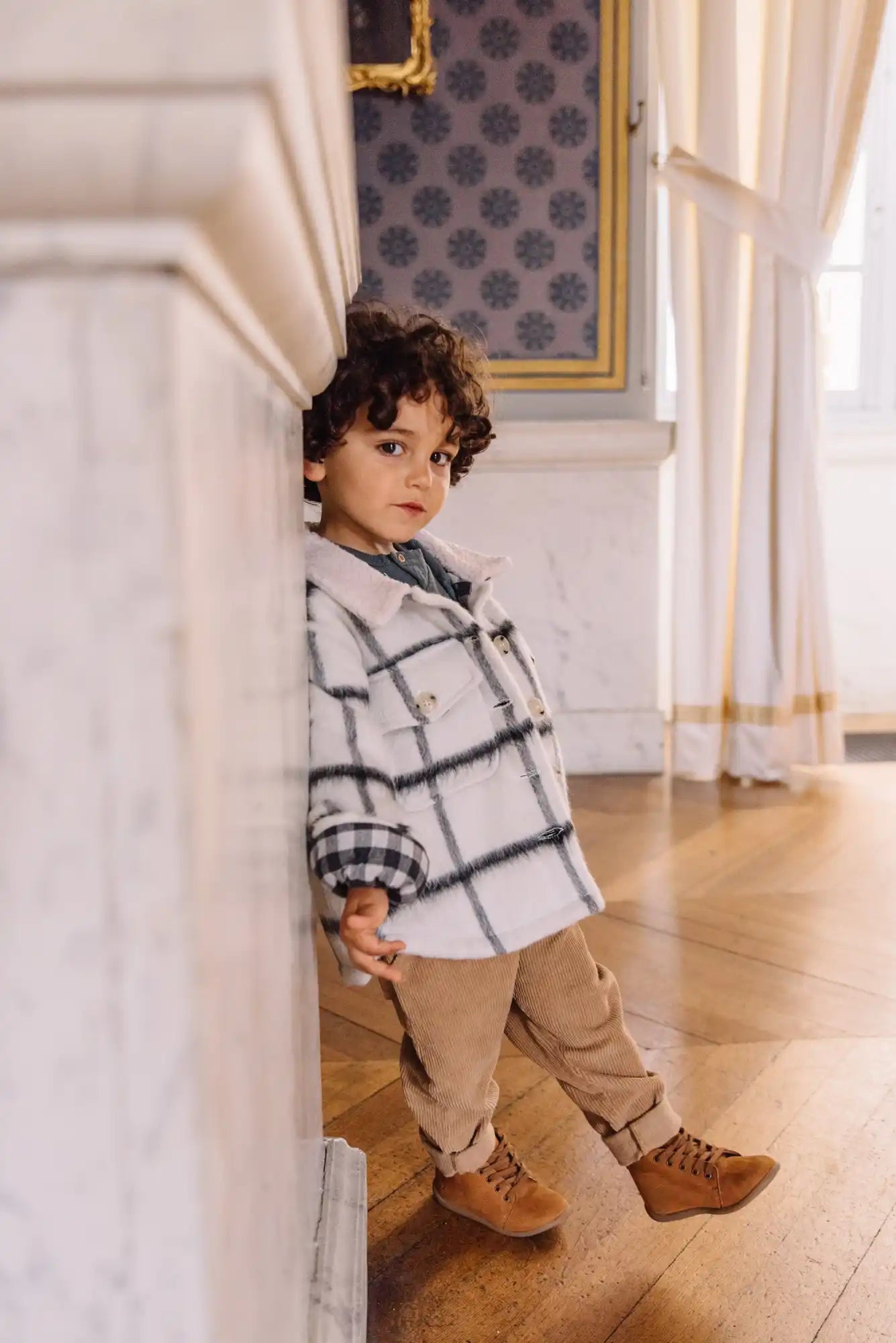 Un jeune enfant portant un pull à carreaux, un pantalon kaki et des bottes marron.