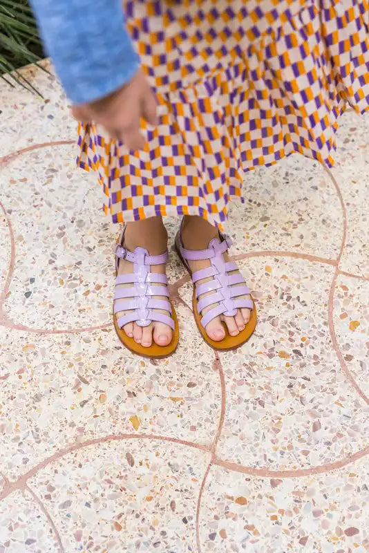 Sandales gladiateurs en cuir lilas avec plusieurs brides portées avec une robe à carreaux.