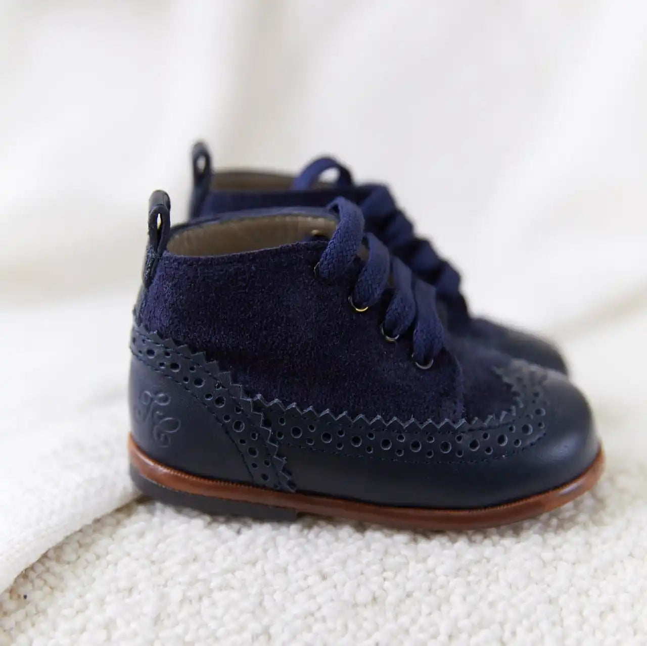 Bottines pour bébé en cuir bleu marine avec des détails brogue décoratifs et des lacets.