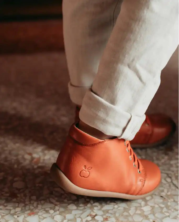 Bottines en cuir orange avec des lacets blancs et des détails de couture.