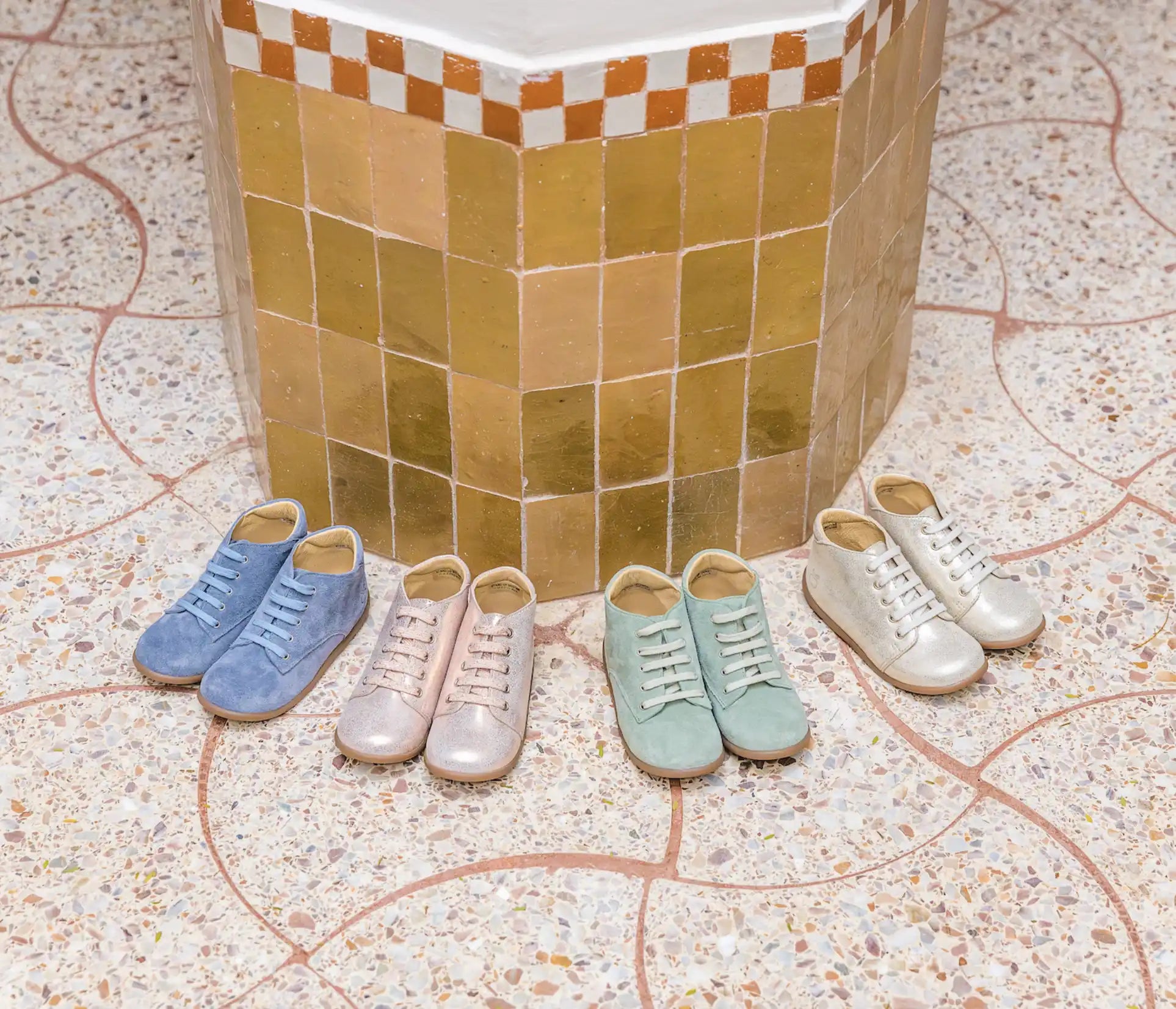 Quatre paires de baskets de couleur pastel disposées en demi-cercle contre un mur carrelé.