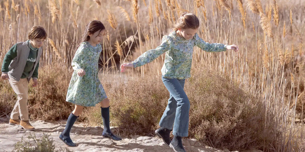 Trois enfants marchant en ligne le long d'un chemin étroit en terre tout en portant des vêtements décontractés.